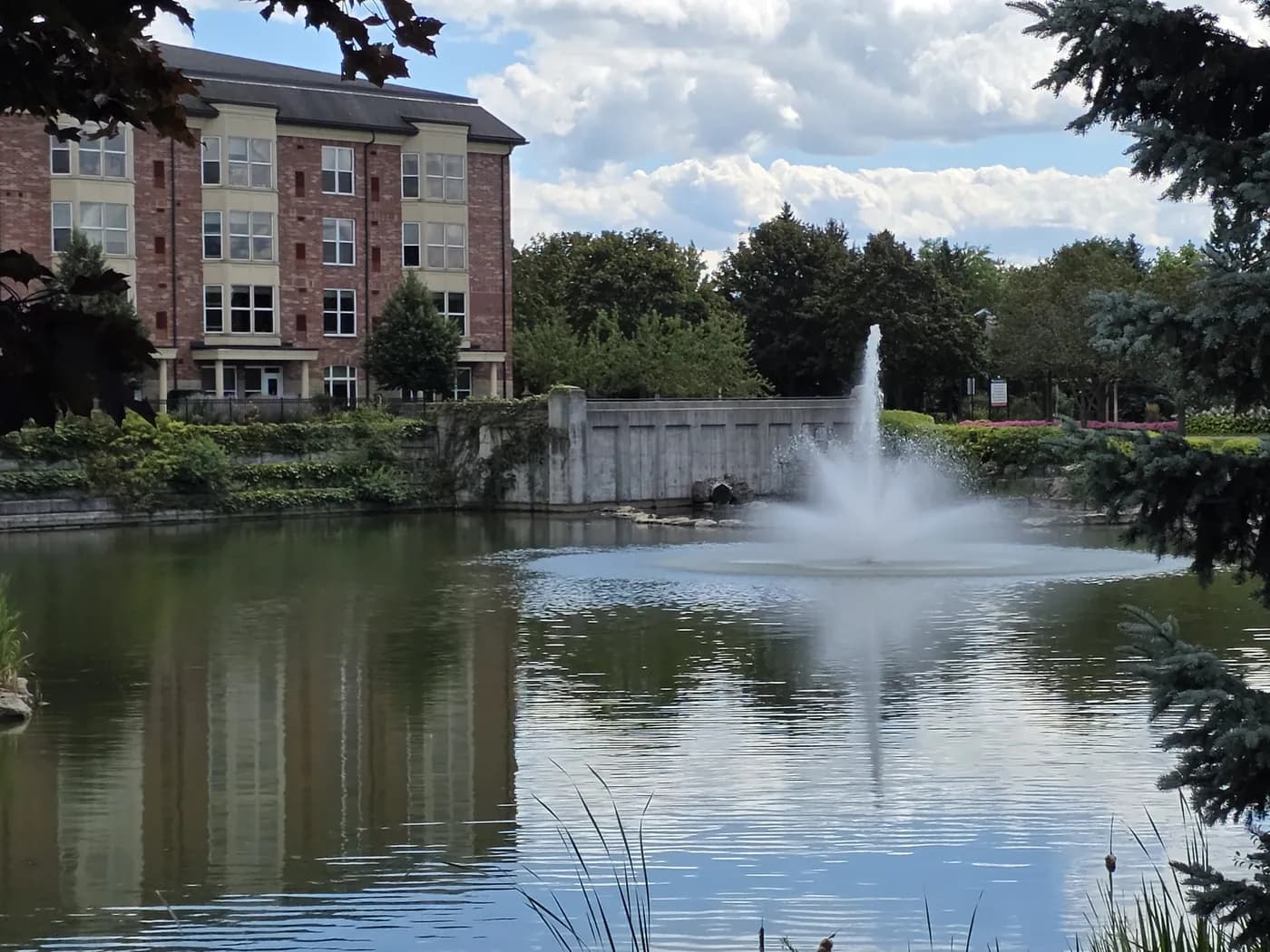 The fountain on the pond at the Village by the Arboretum in Guelph, with resident buildings behind it.