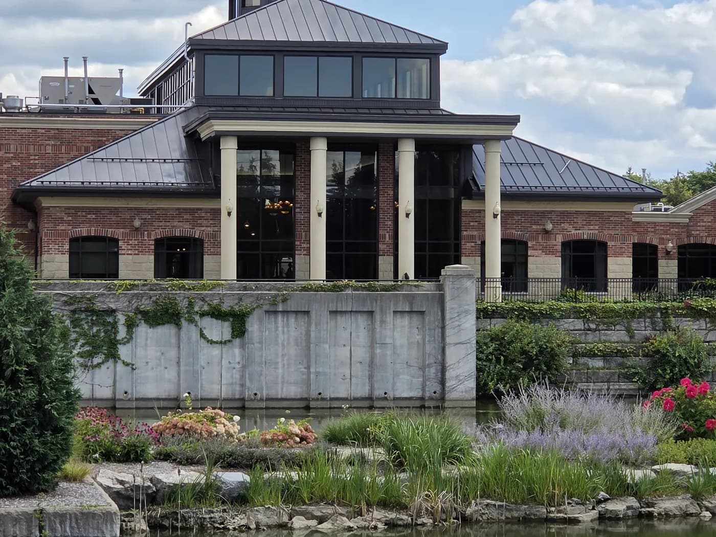 The Village Centre building at the Village by the Arboretum in Guelph, seen across the pond with gardens in the foreground.